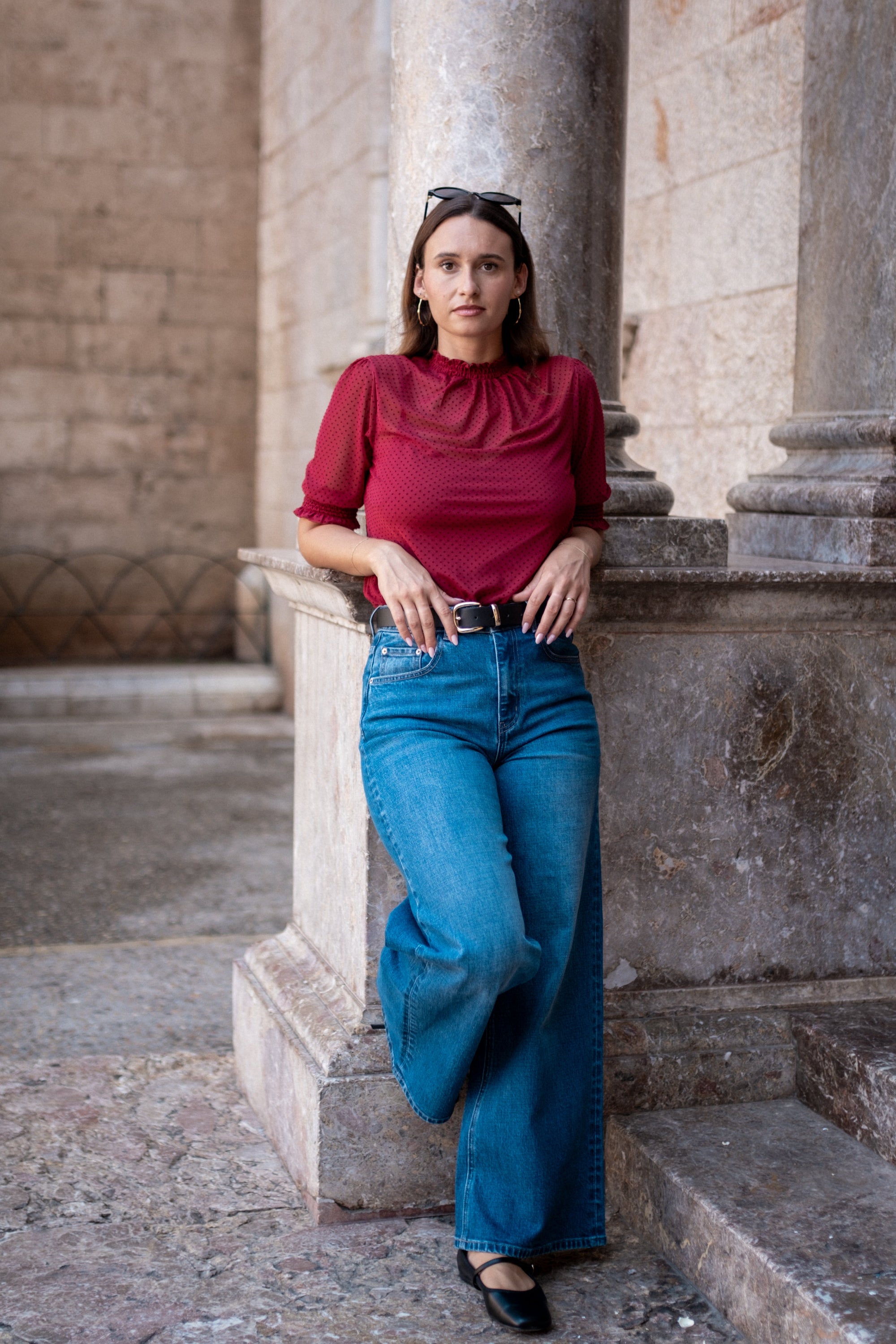 Woman in a red top and blue jeans standing on stone steps with columns in the background