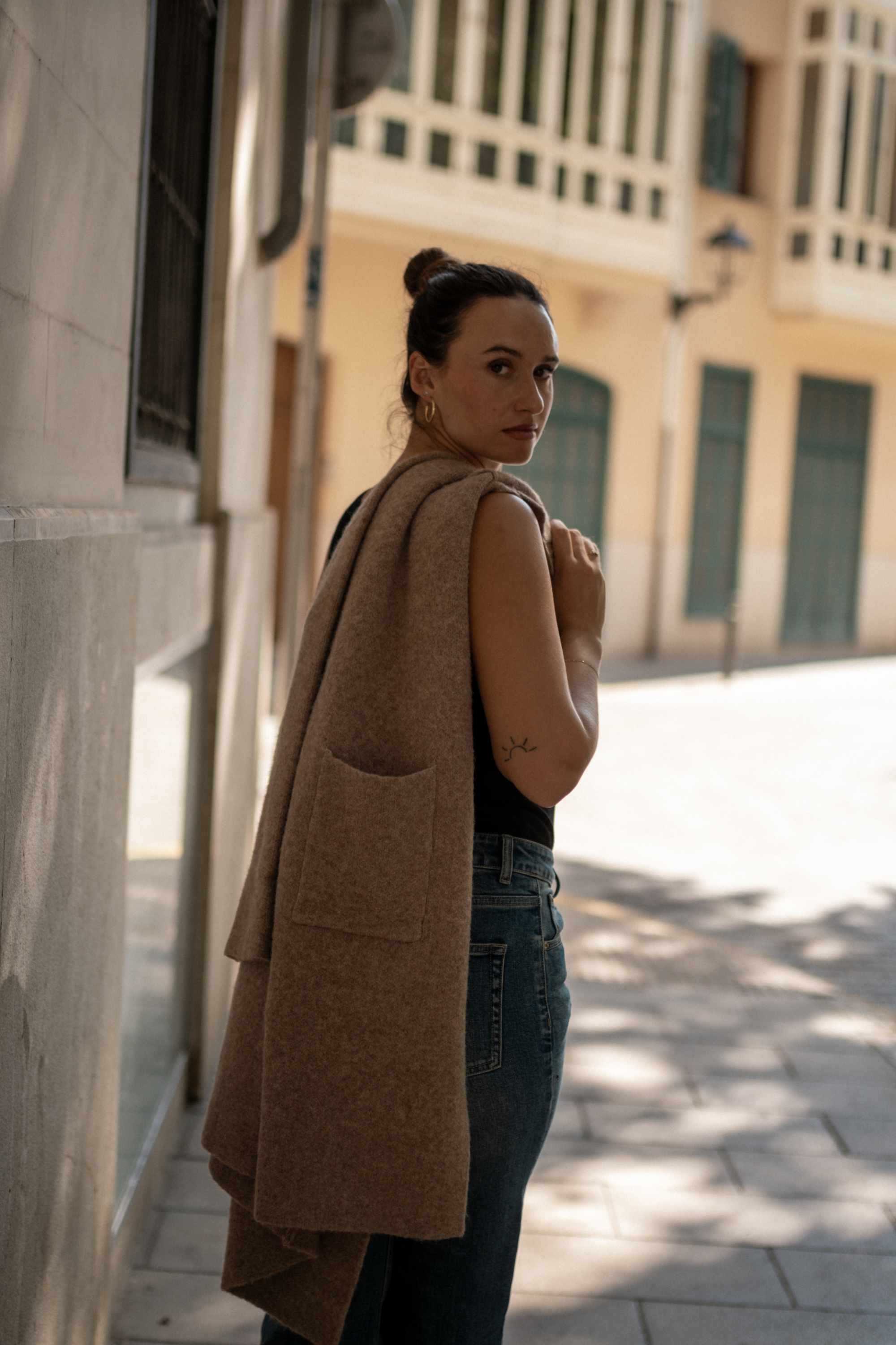 Woman wearing a beige coat standing on a street with buildings in the background