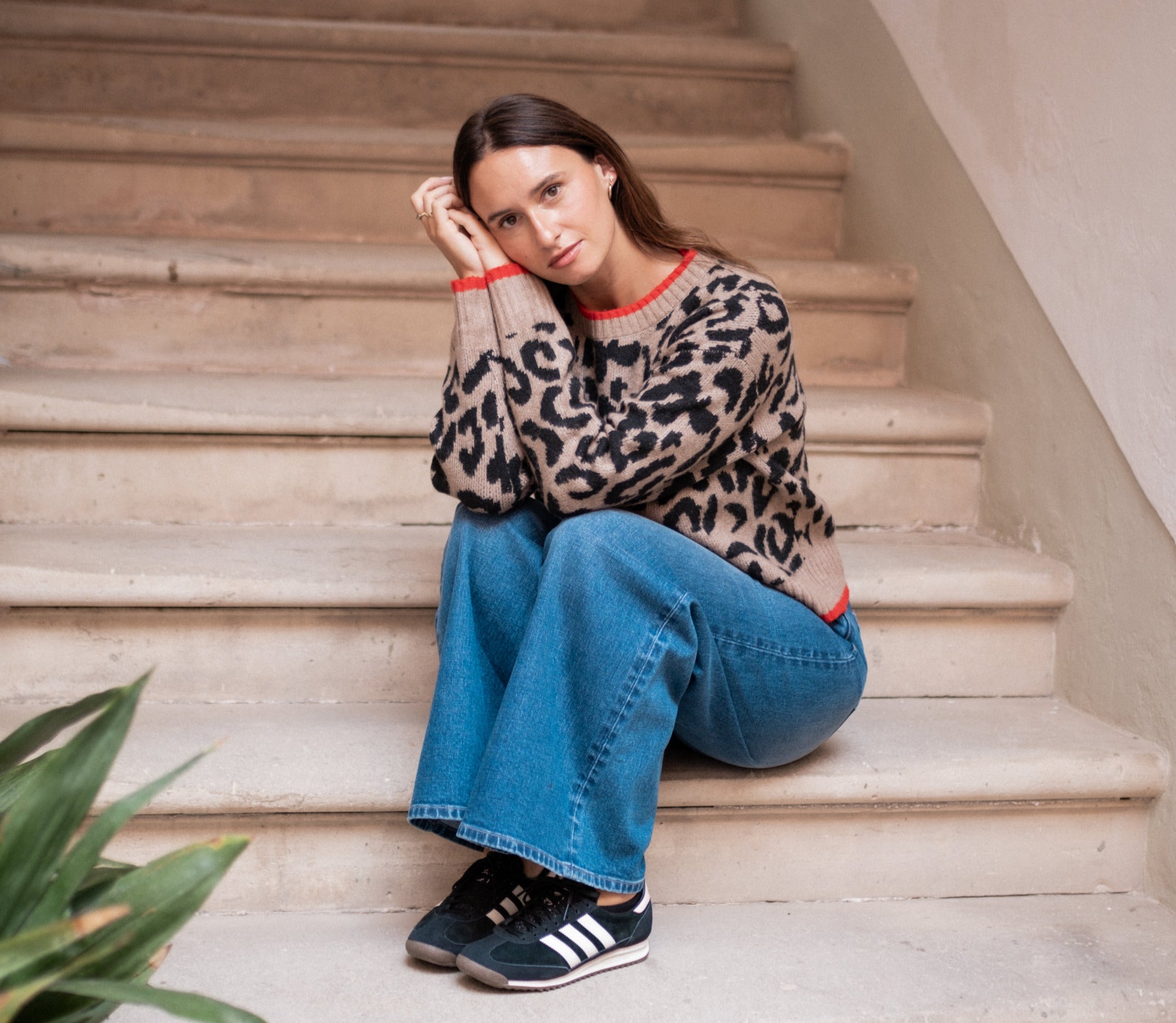 Woman sitting on a staircase wearing a leopard print sweater and blue jeans.