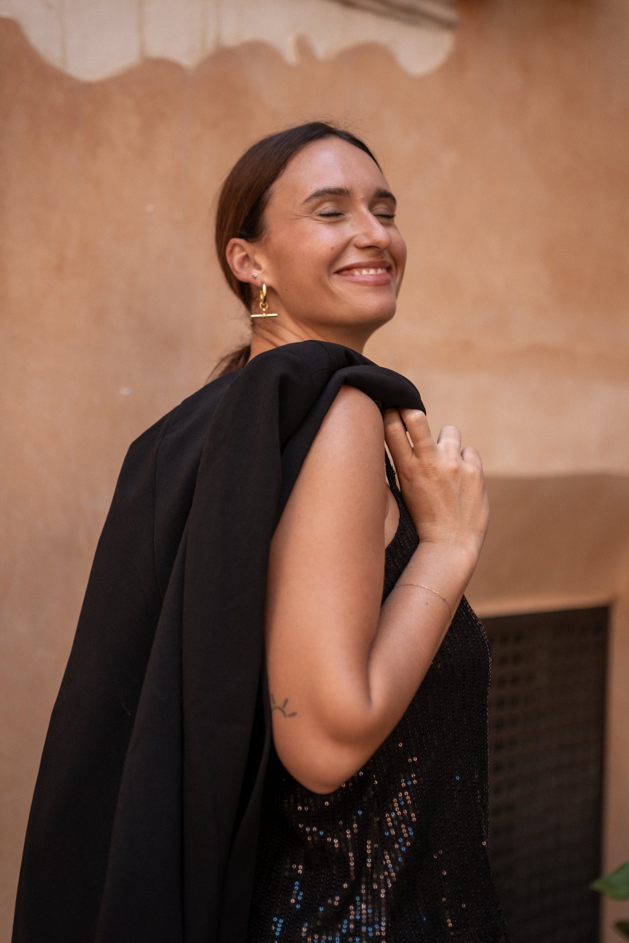 Woman wearing a black blazer over a sequin top against a beige wall