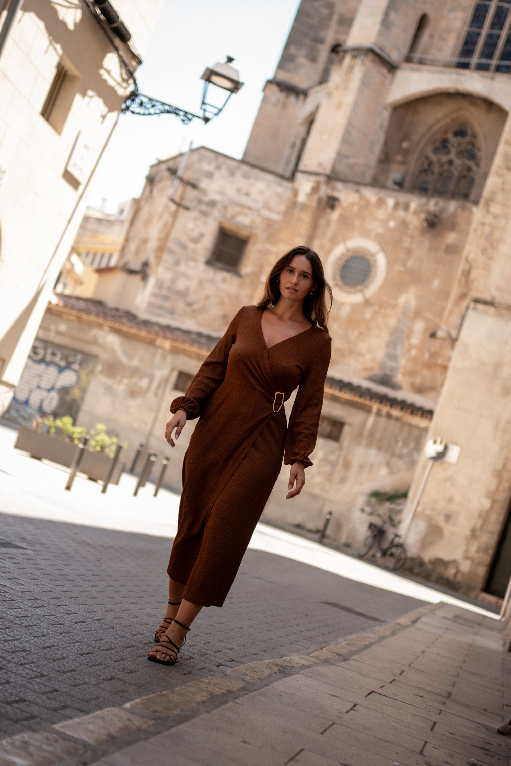 Woman in a brown dress walking in front of a cathedral