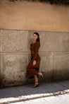 Woman in a brown dress standing against a textured wall.