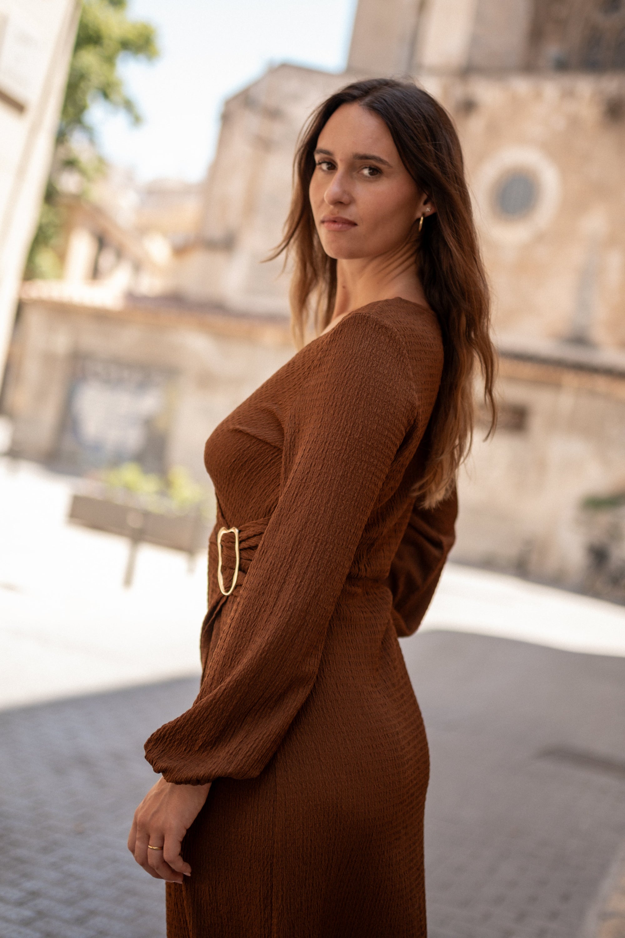 Woman in a brown dress standing outdoors with a blurred background