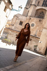 Woman in a brown dress walking in front of a cathedral
