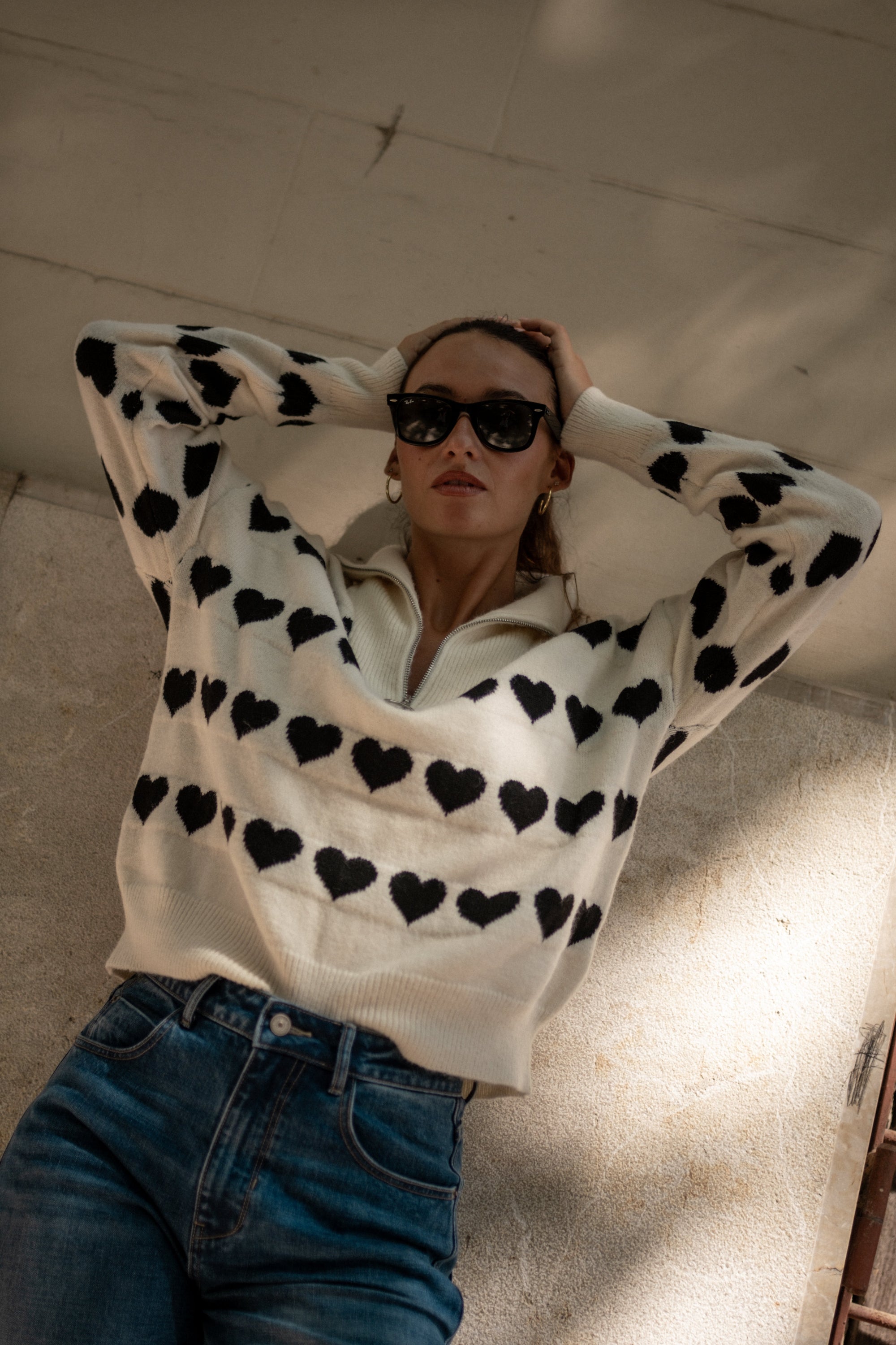 Woman wearing a white sweater with black heart patterns and blue jeans.