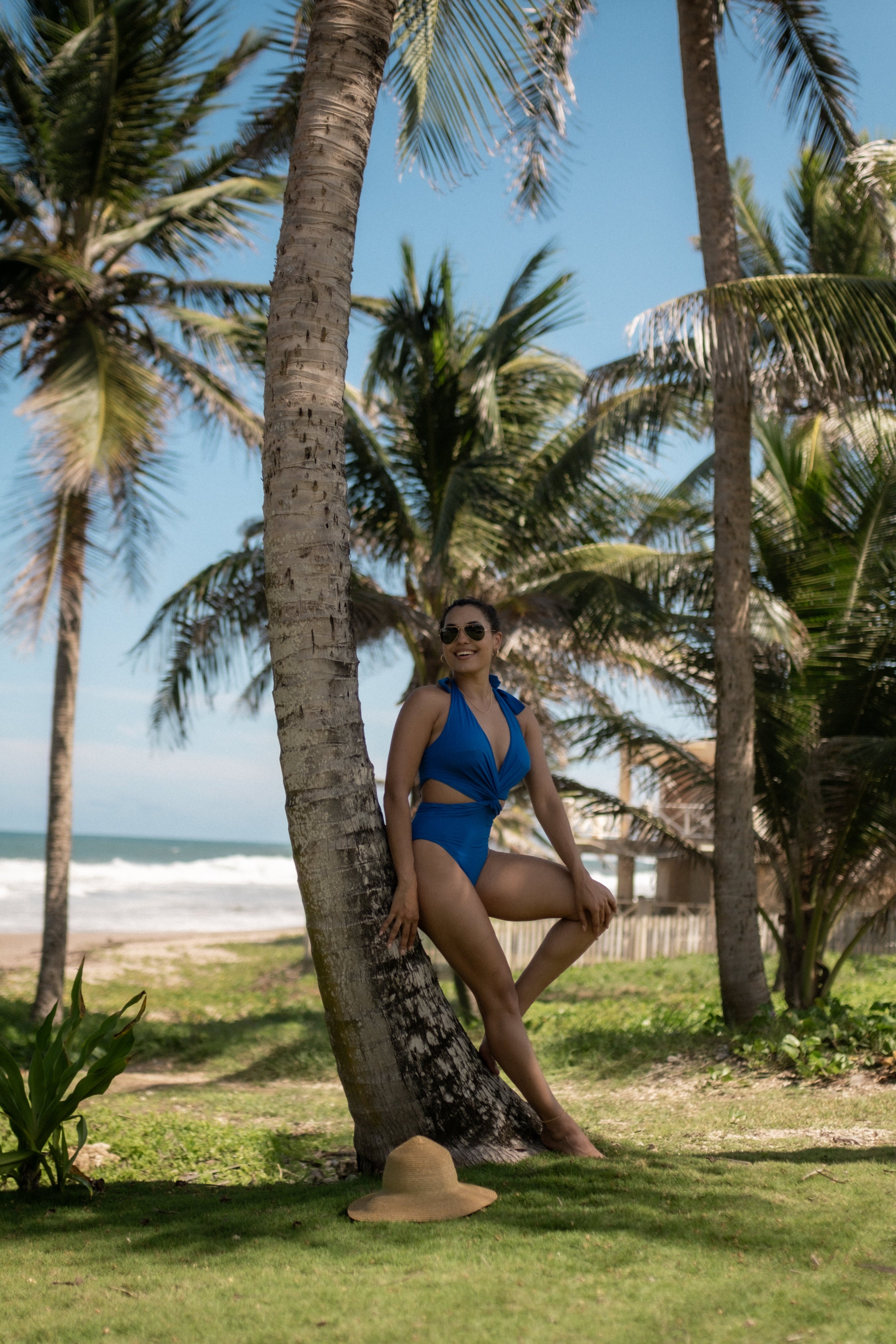 Woman in a blue swimsuit leaning against a palm tree on a beach