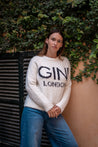 Person wearing a white sweater with 'GINI LONDON' text against a green leafy background