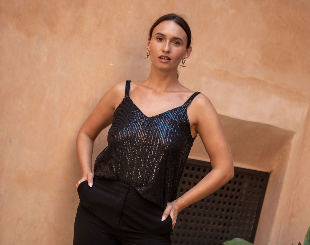 Woman wearing a black sequin top against a beige wall